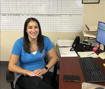 Female Employee with brown hair looking at camera at her desk 